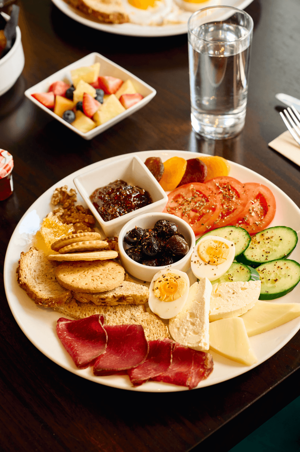 Plate of complimentary breakfast featuring cured meats, cheeses, fresh vegetables, bread, soft-boiled eggs, and a side of fresh fruit.