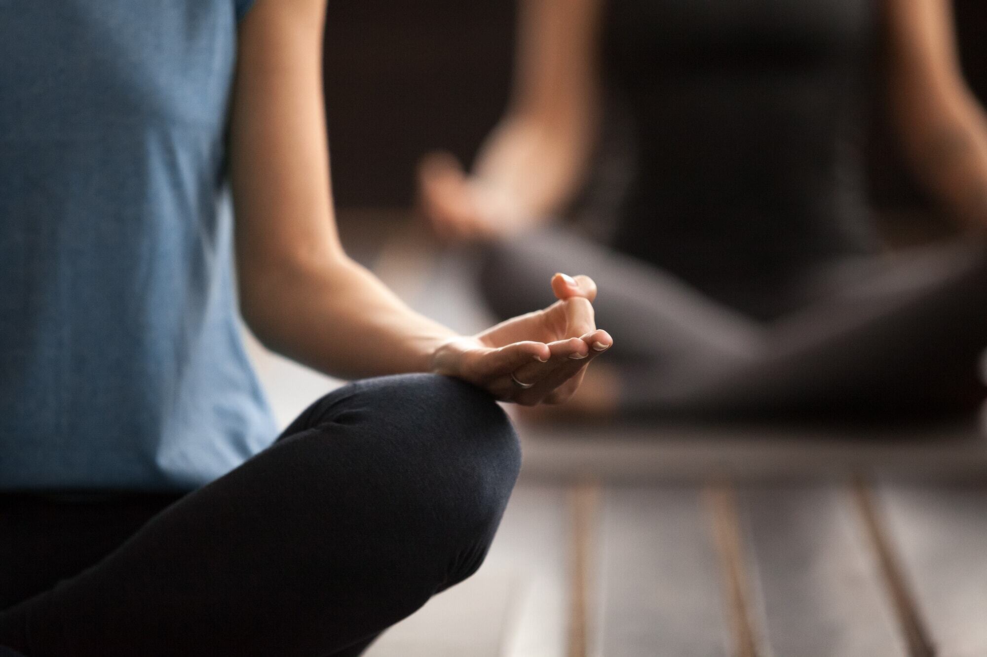 Person sitting cross-legged on a yoga mat with one hand resting on their knee in a meditation pose